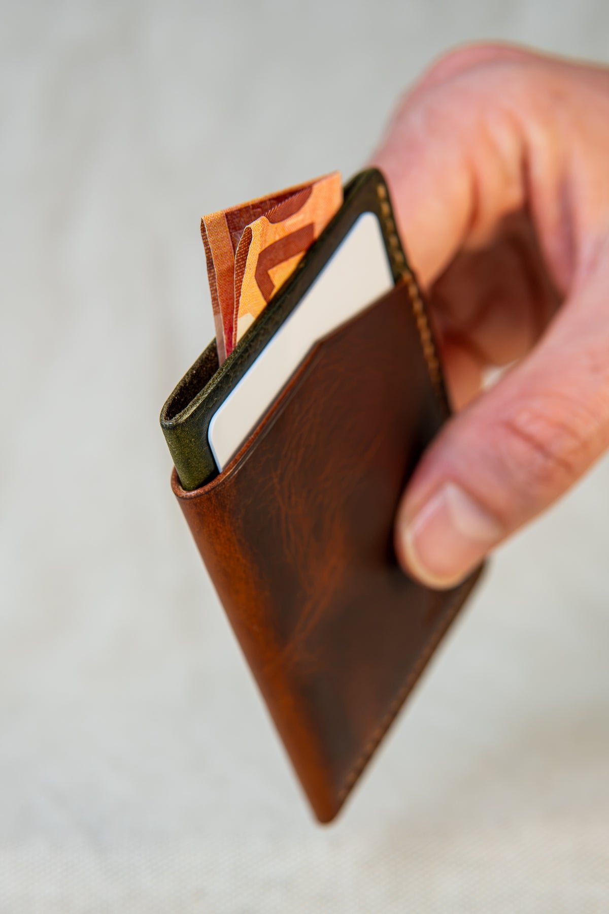 Porte-cartes Bastan en cuir cognac et olive tenu en main, format compact