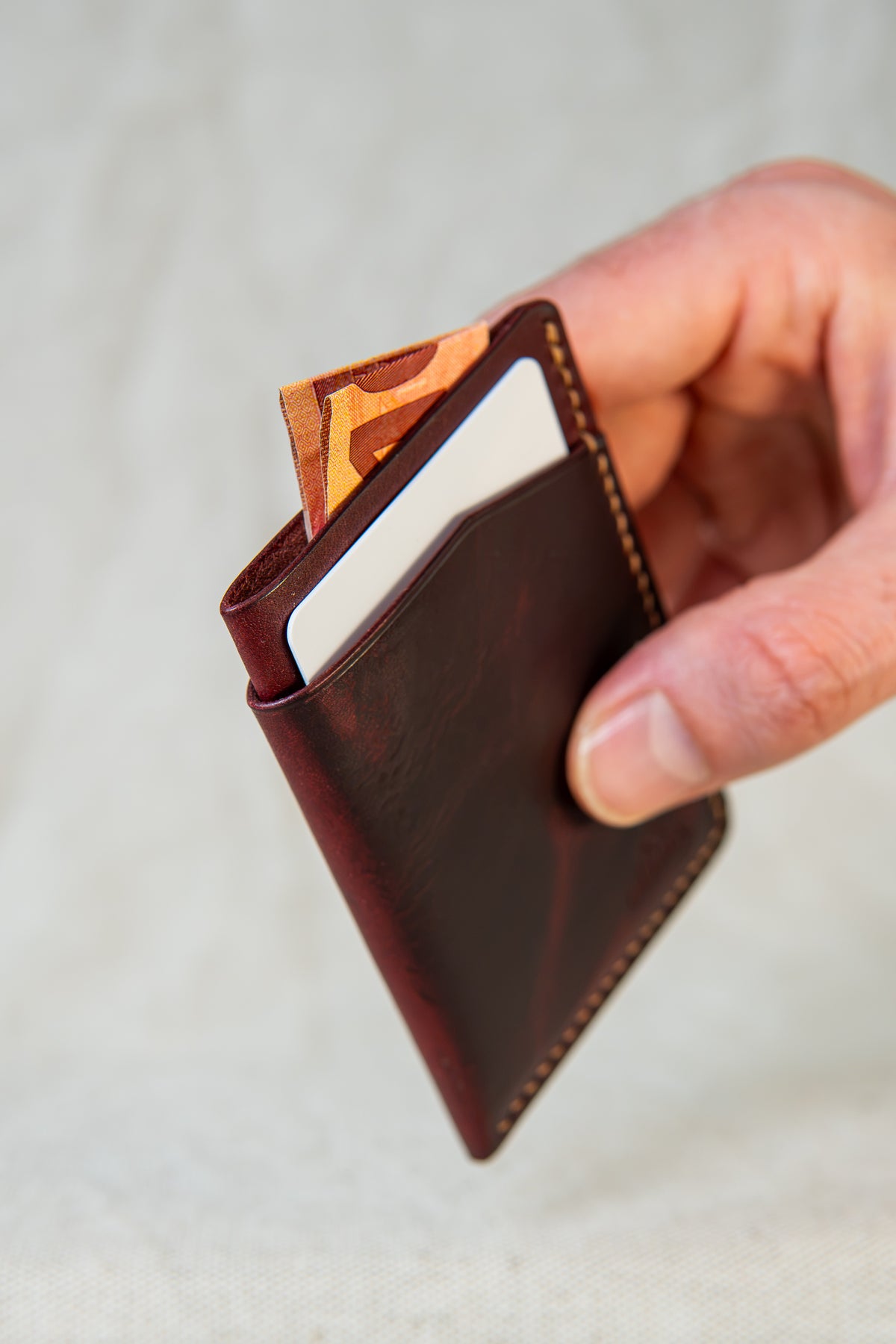 Porte-cartes Bastan en cuir bordeaux et bourgogne, tenu en main avec carte et billet