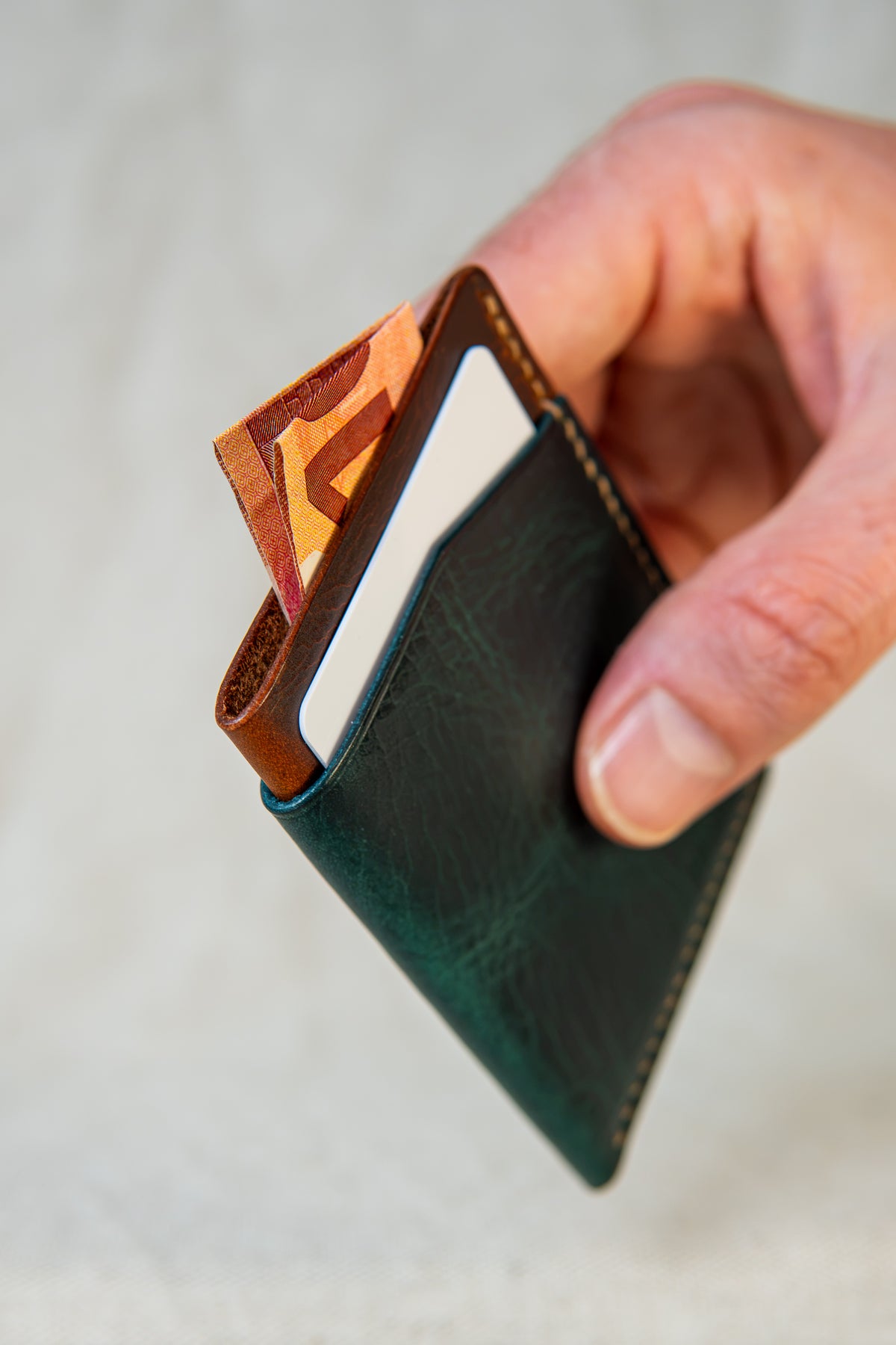 Porte-cartes Bastan en cuir turquoise et cognac, tenu en main