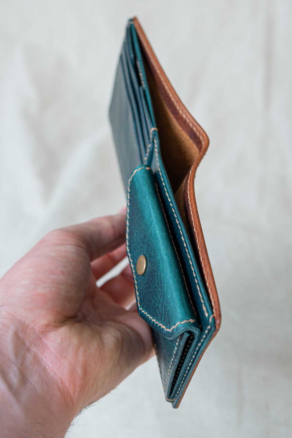 Portefeuille Vignemale en cuir cognac et turquoise, tenu en main ouvert