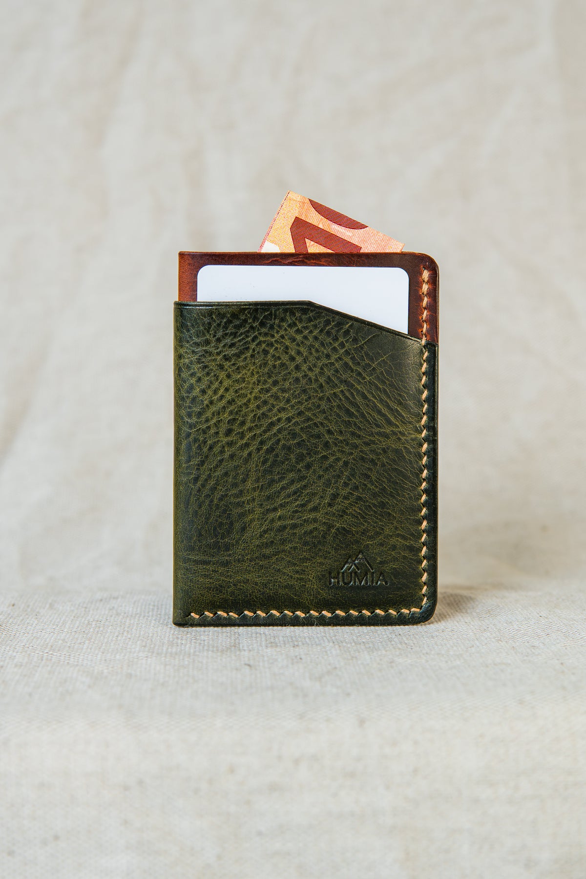 Porte-cartes Bastan en cuir olive et cognac tenu en main, format compact