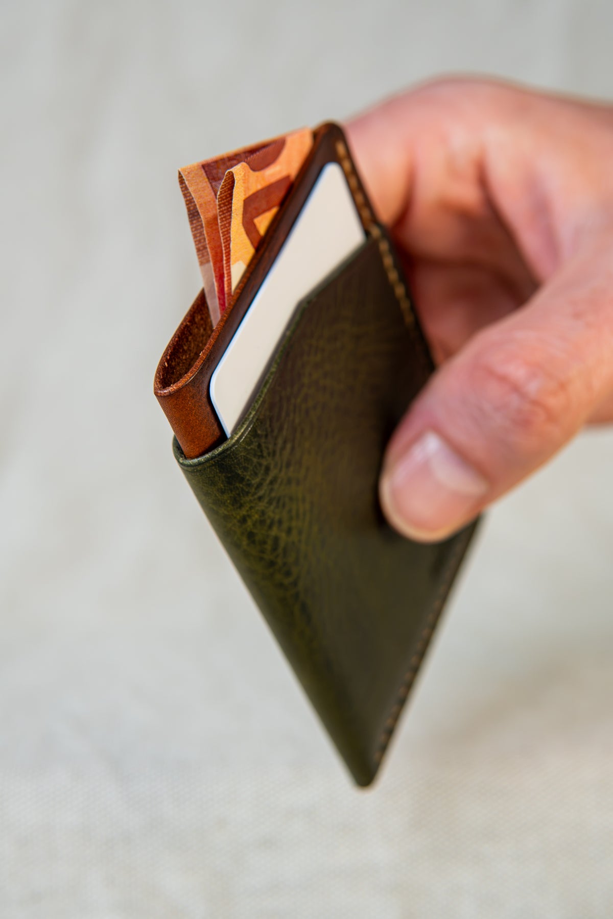 Porte-cartes Bastan en cuir olive et cognac, tenu en main