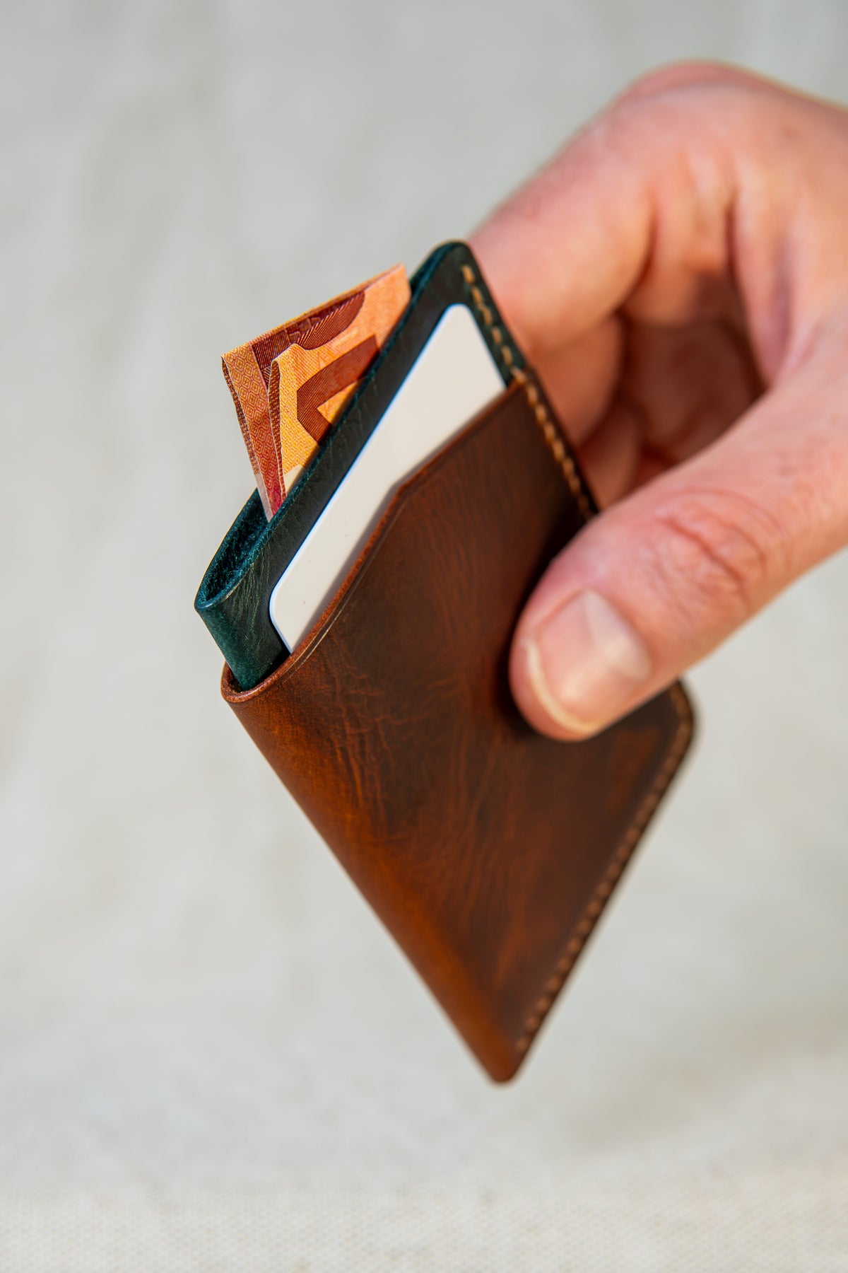 Porte-cartes Bastan en cuir cognac et turquoise, tenu en main avec carte et billet