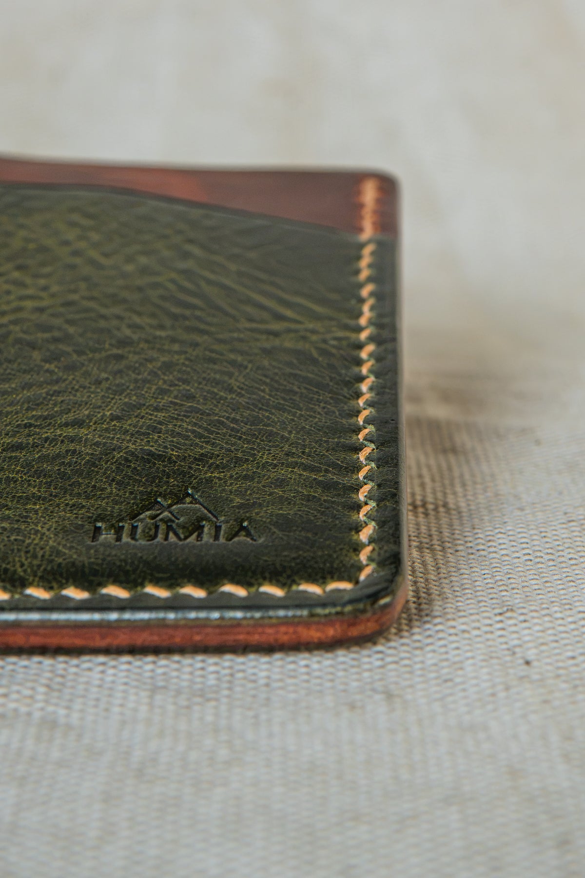 Détail de la couture main au point sellier du porte-cartes Bastan en cuir olive et cognac