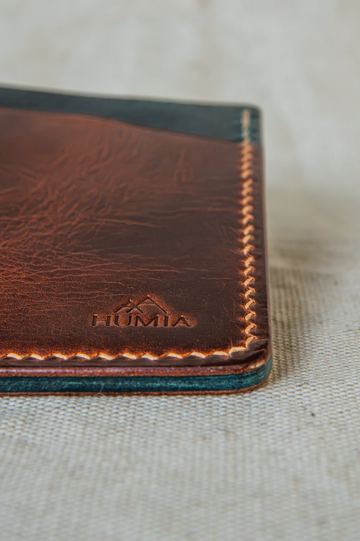 Détail de la couture main au point sellier du porte-cartes Bastan en cuir cognac et turquoise
