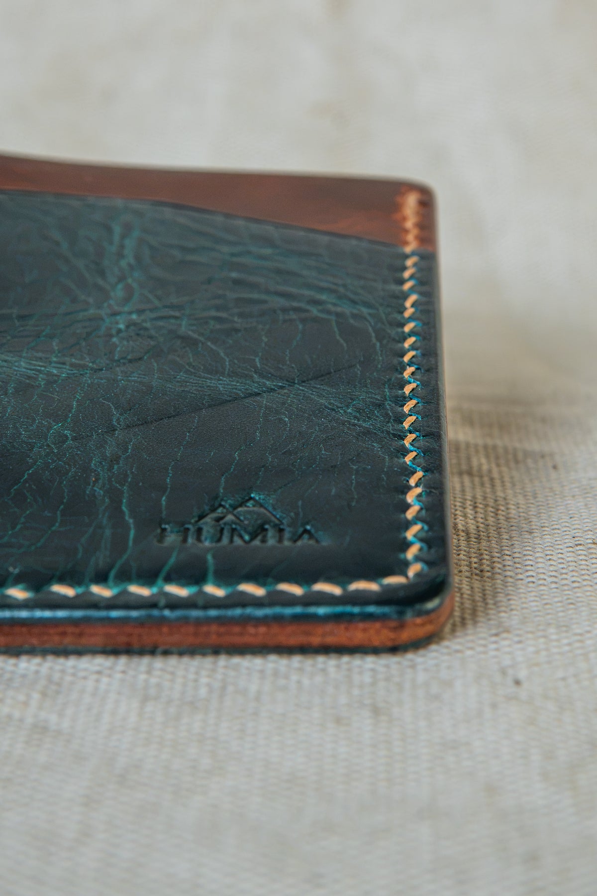 Détail de la couture main au point sellier du porte-cartes Bastan en cuir turquoise et cognac