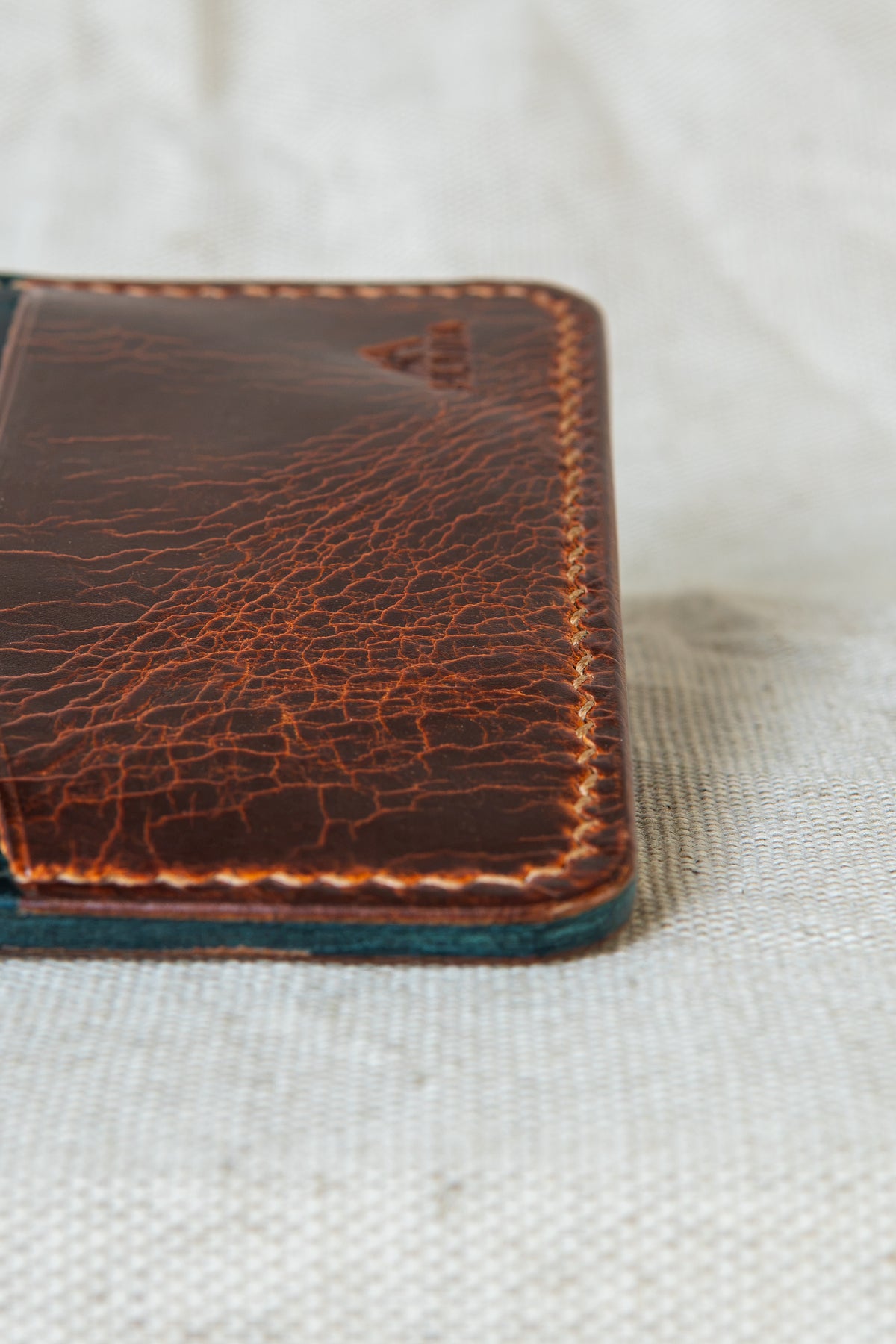 Détail de la couture main au point sellier du porte-cartes Hautacam en cuir cognac et turquoise