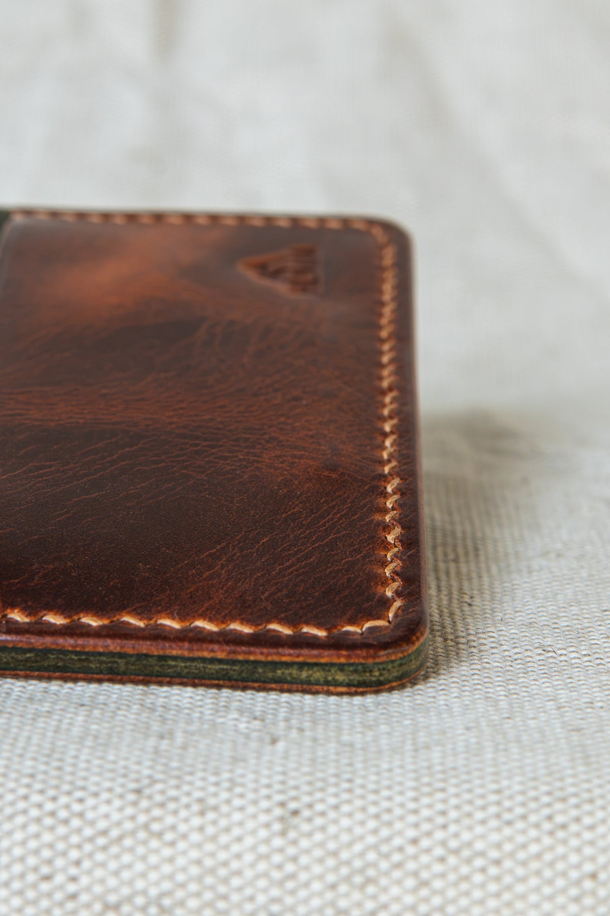 Détail de la couture main au point sellier du porte-cartes Hautacam en cuir cognac et olive