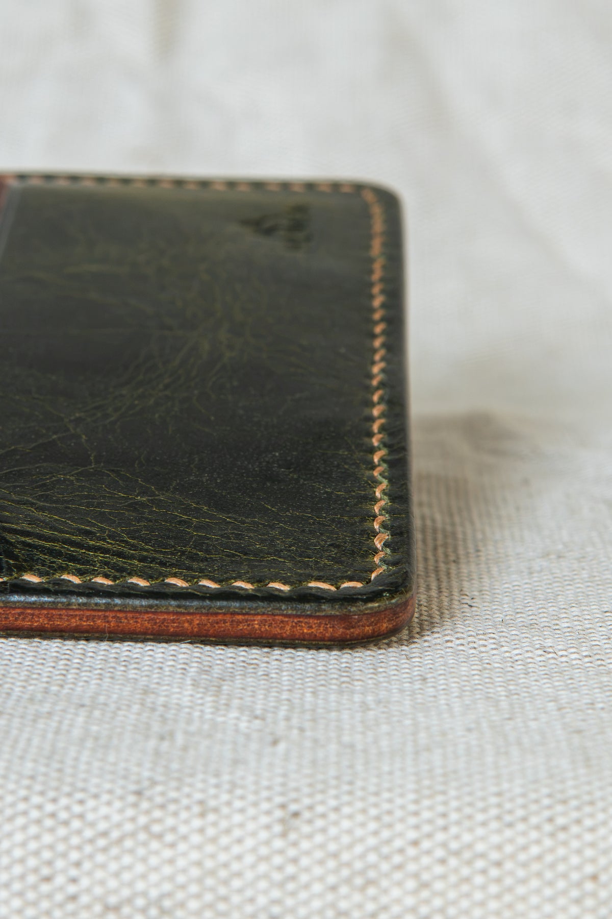 Détail de la couture main au point sellier du porte-cartes Hautacam en cuir olive et cognac
