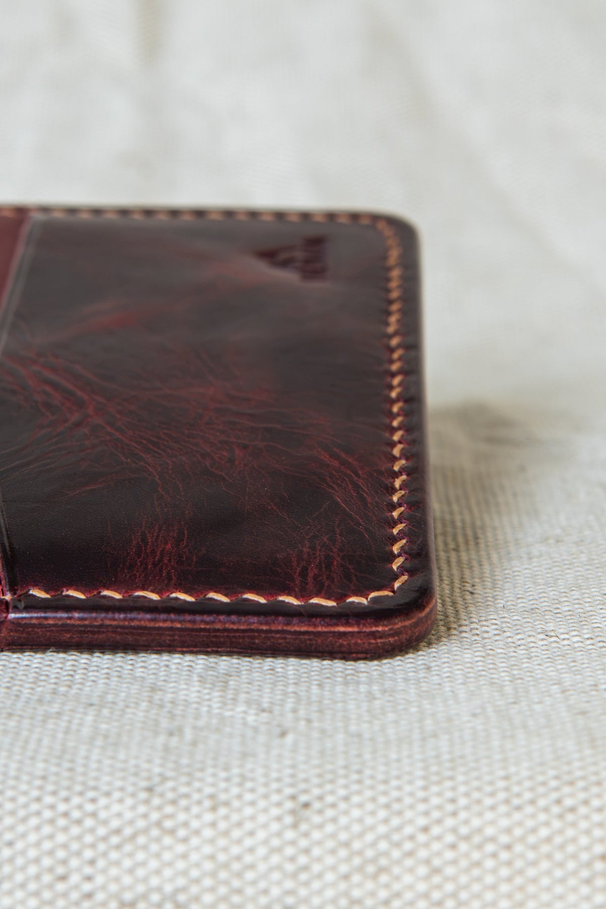 Détail de la couture main au point sellier du porte-cartes Hautacam en cuir bordeaux et bourgogne