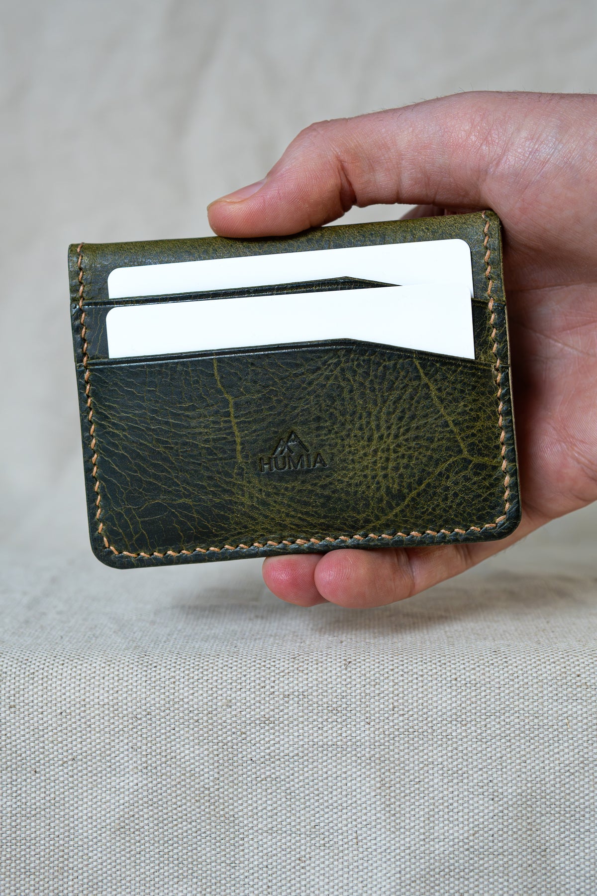 Porte-cartes Soulor en cuir olive, tenu en main vue de face avec cartes
