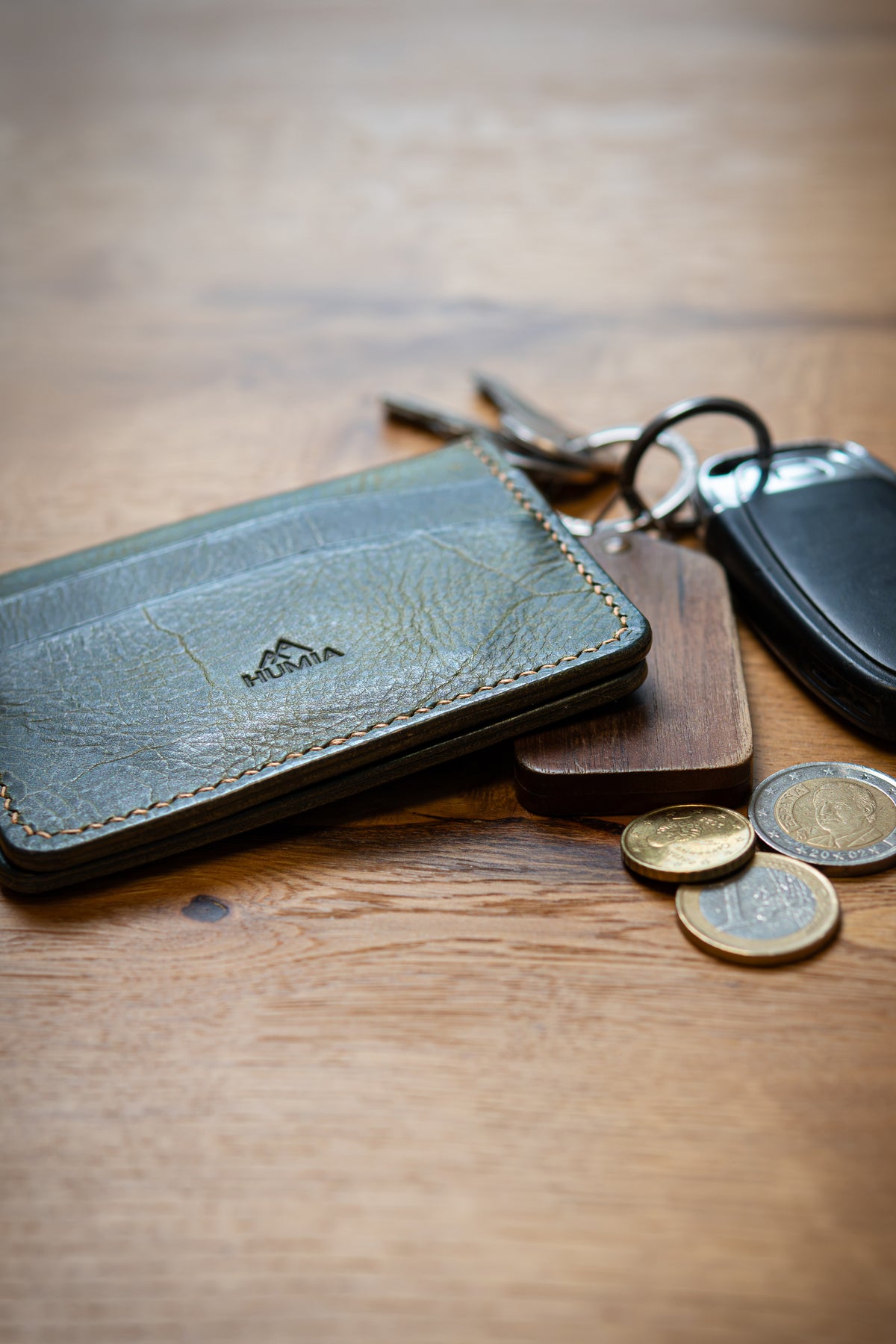 Porte-cartes Soulor en cuir olive, posé sur une table avec clés et pièces de monnaie