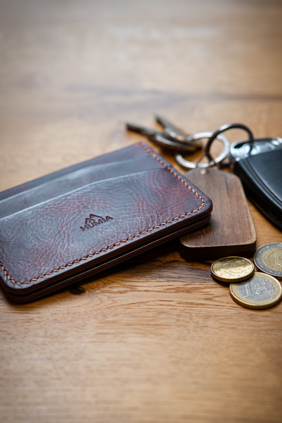 Porte-cartes Soulor en cuir bordeaux, posé sur une table en bois avec clé et pièces de monnaie
