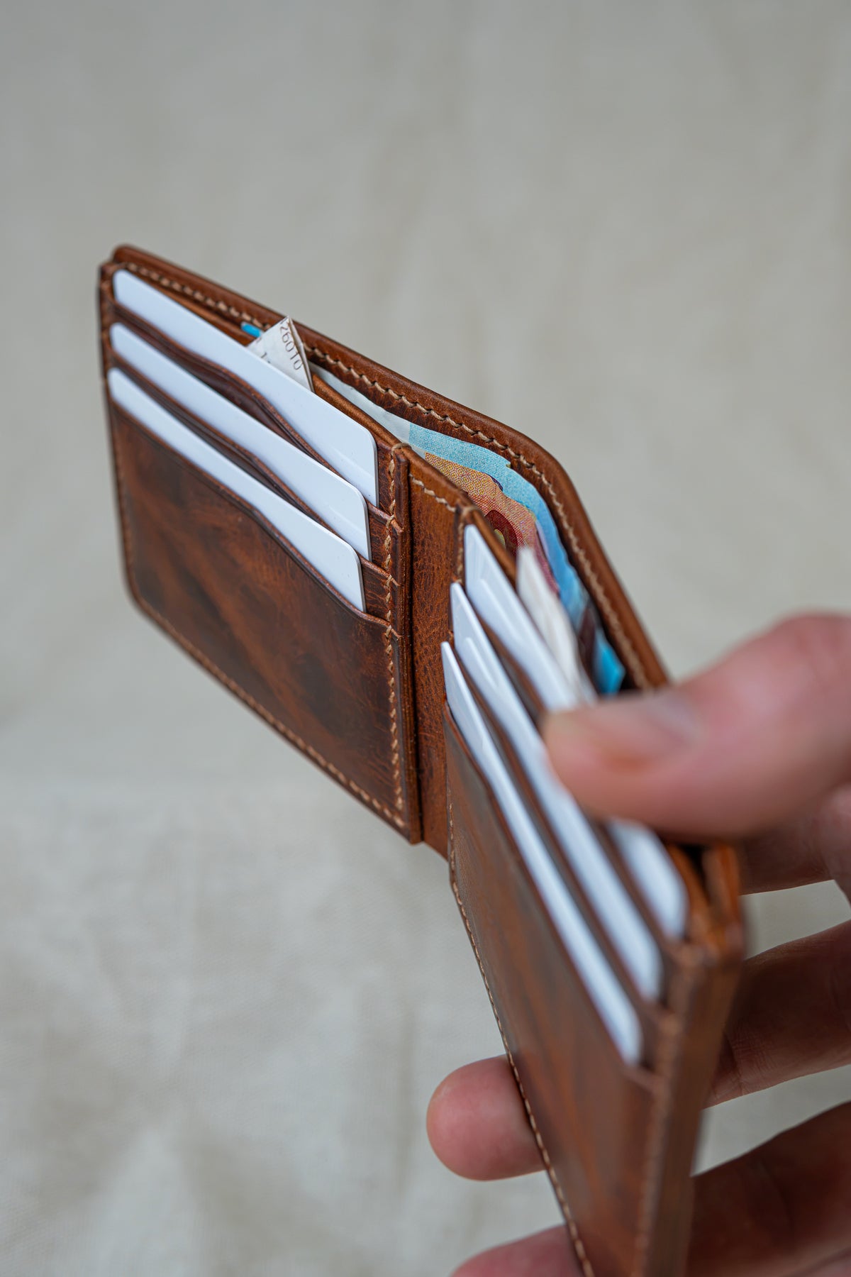Portefeuille Tourmalet en cuir cognac, tenu en main ouvert avec cartes et billets