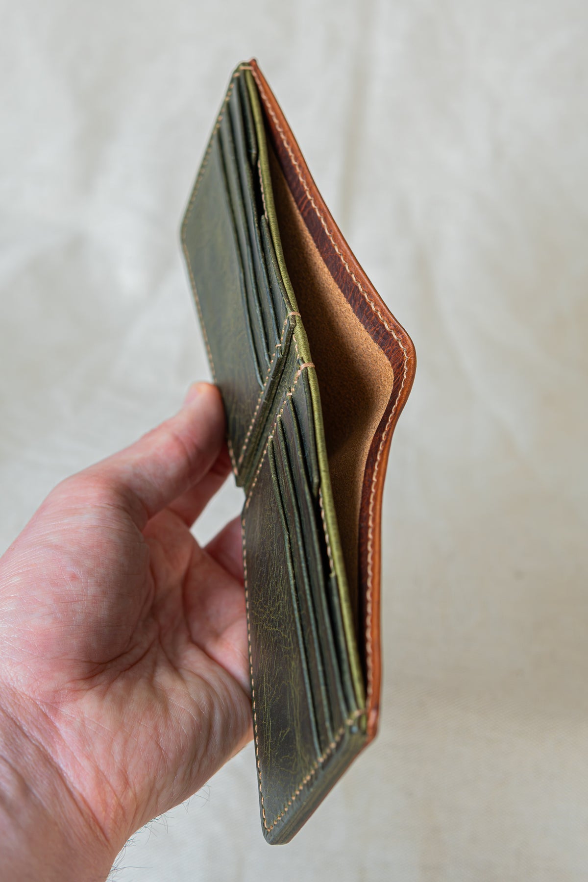 Portefeuille Tourmalet en cuir cognac et olive, tenu dans la main