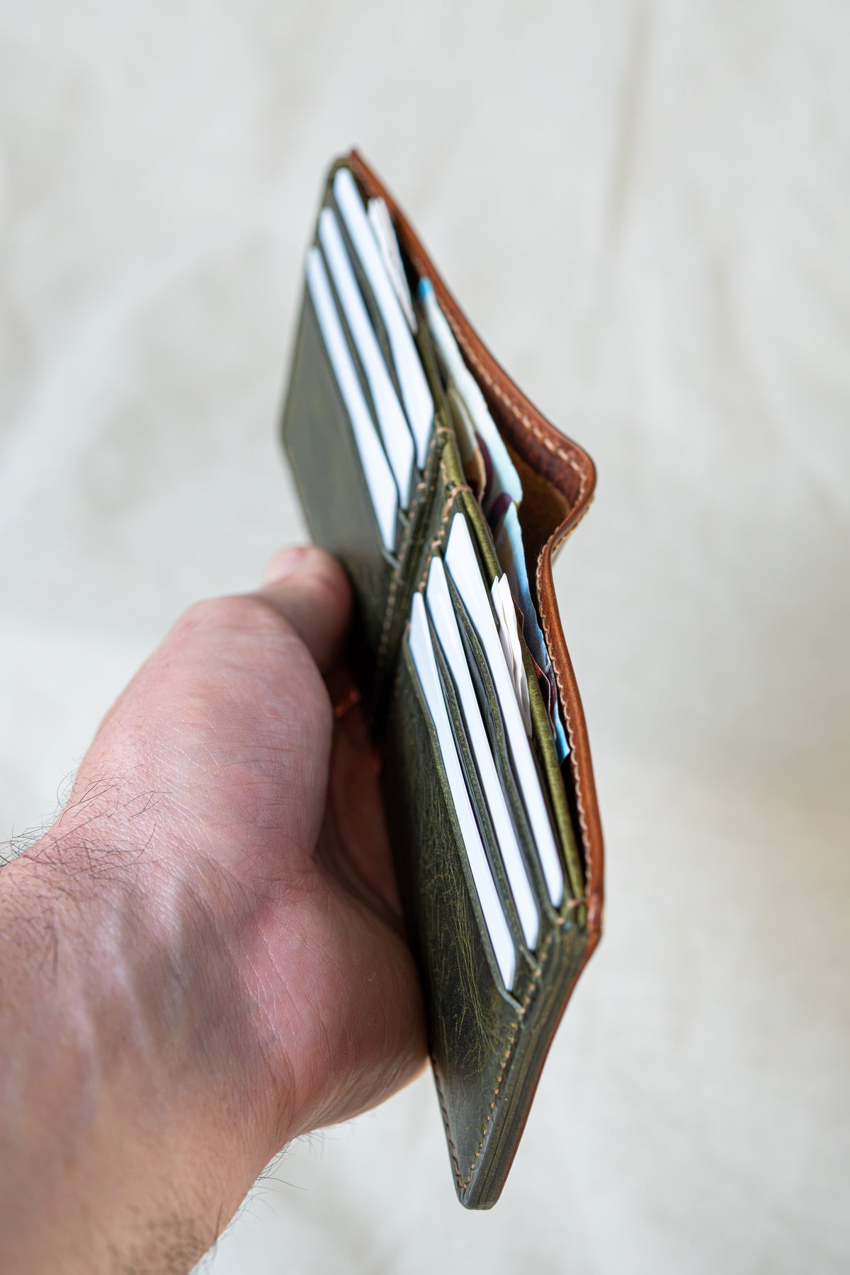 Portefeuille Tourmalet en cuir cognac et olive, tenu dans la main avec cartes et billets