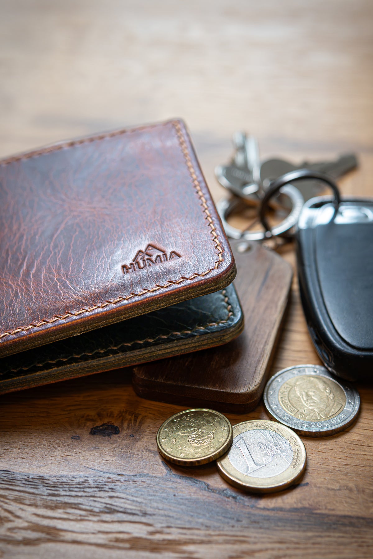 Portefeuille Tourmalet en cuir cognac et olive, posé sur table bois avec clé et pièces de monnaie