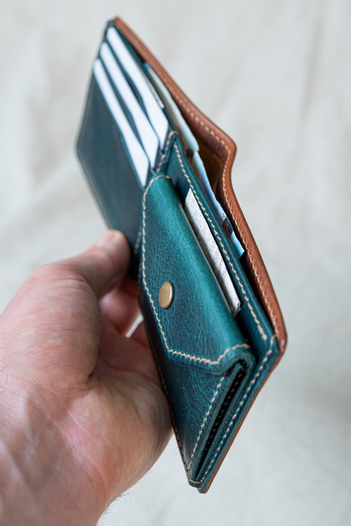 Portefeuille Vignemale en cuir cognac et turquoise, tenu en main avec cartes et billets