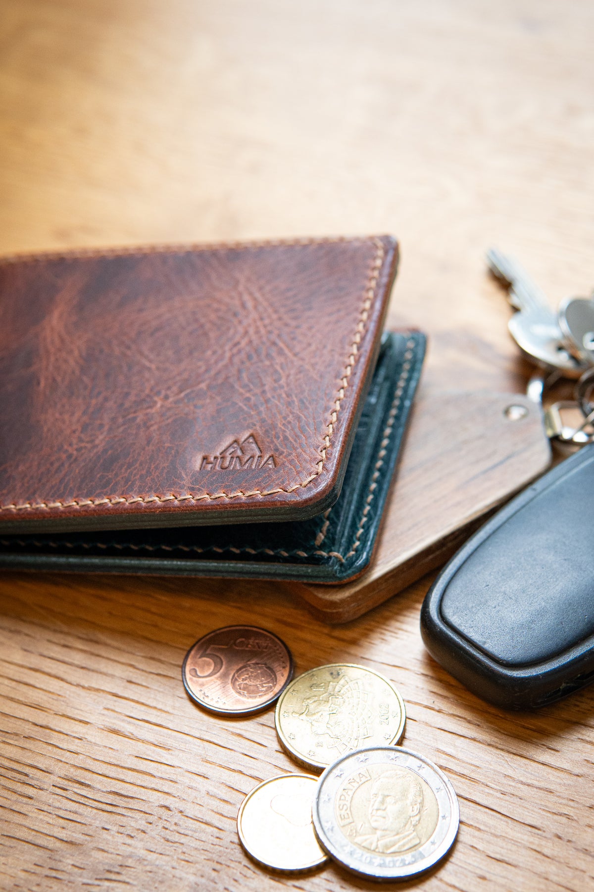 Portefeuille Vignemale en cuir cognac et turquoise, posé sur table bois avec clés et pièces monnaie
