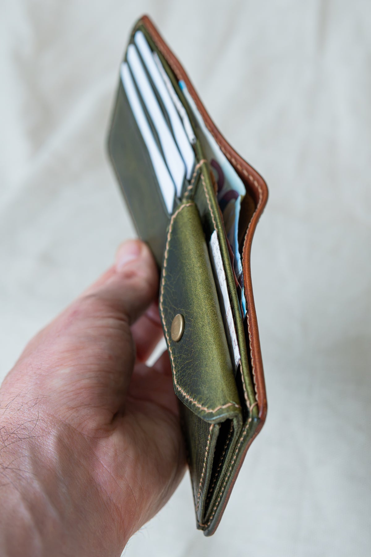 Portefeuille Vignemale en cuir cognac et olive, tenu en main ouvert avec cartes et billets